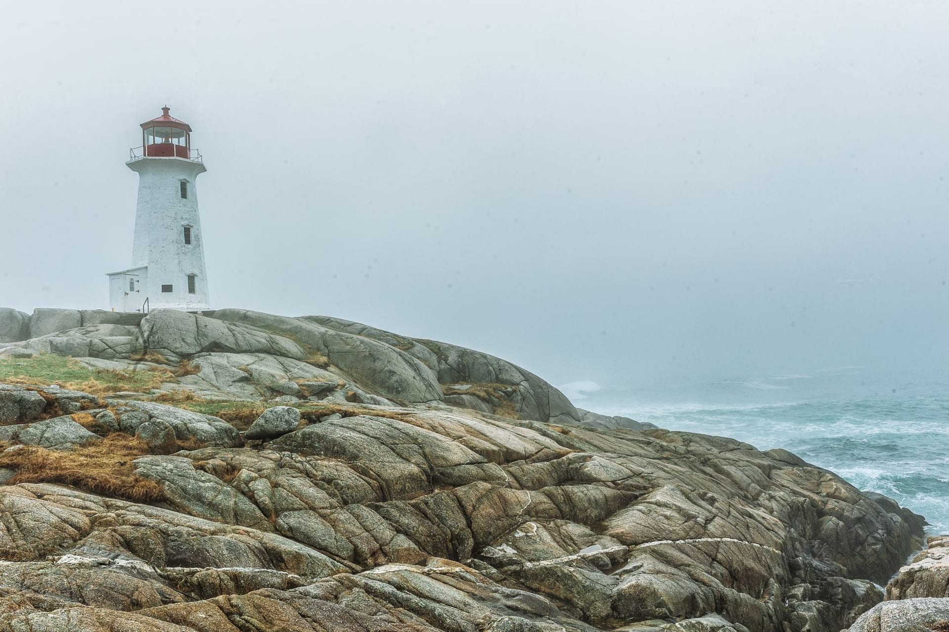 Peggy's Cove lighthouse perched on wave-smoothed granite rocks under a dramatic overcast sky