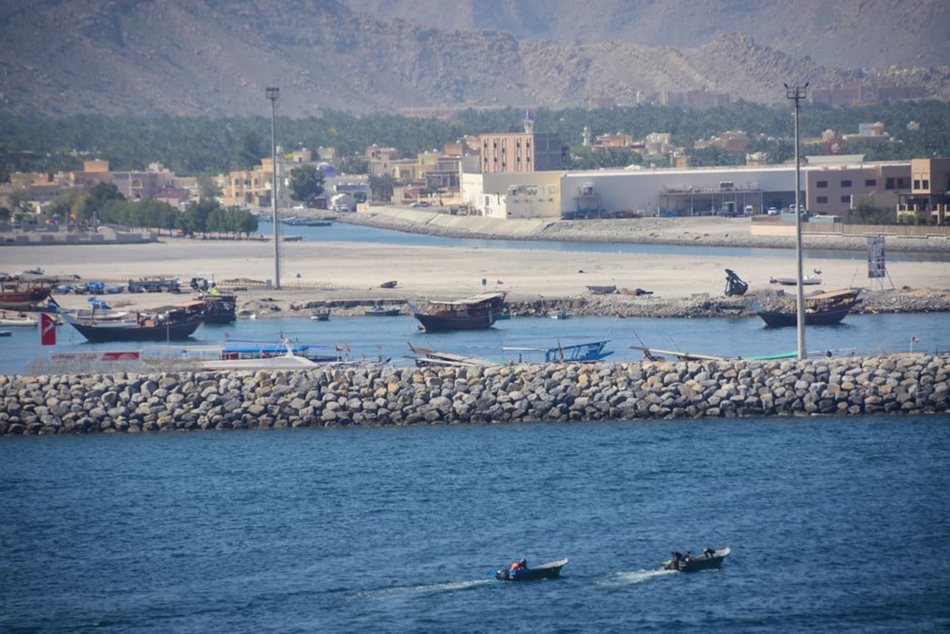 Une ancienne tour de guet omanaise sur un affleurement rocheux au-dessus du littoral du Batinah près d'Al Musanaah, avec des bateaux de pêche visibles dans la baie en contrebas