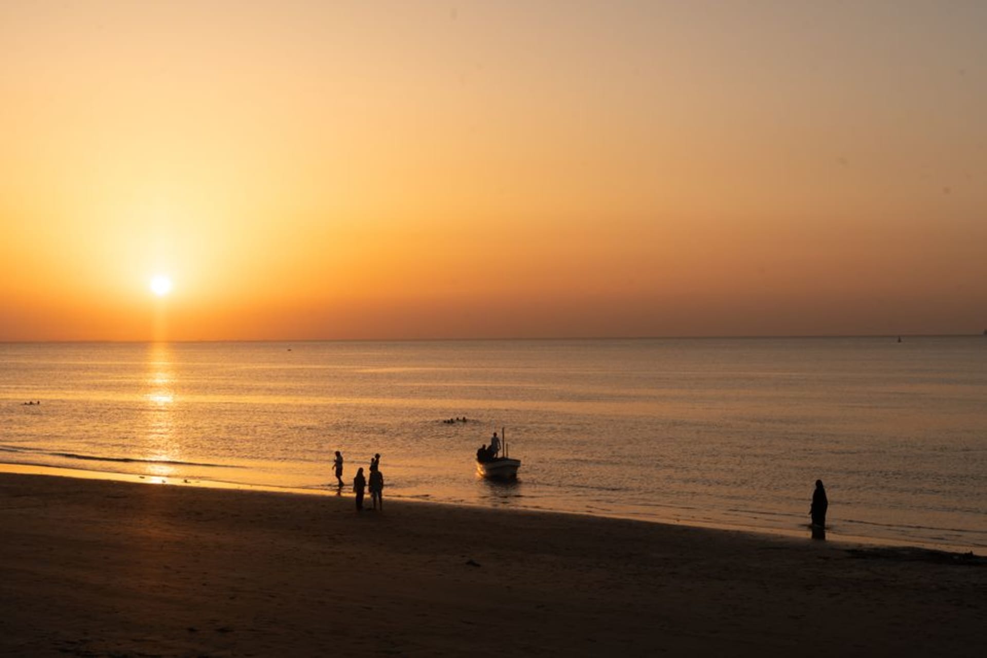 Wide, empty beach at Duqm on Oman's central coast with dark cliffs and port cranes visible in the distance.