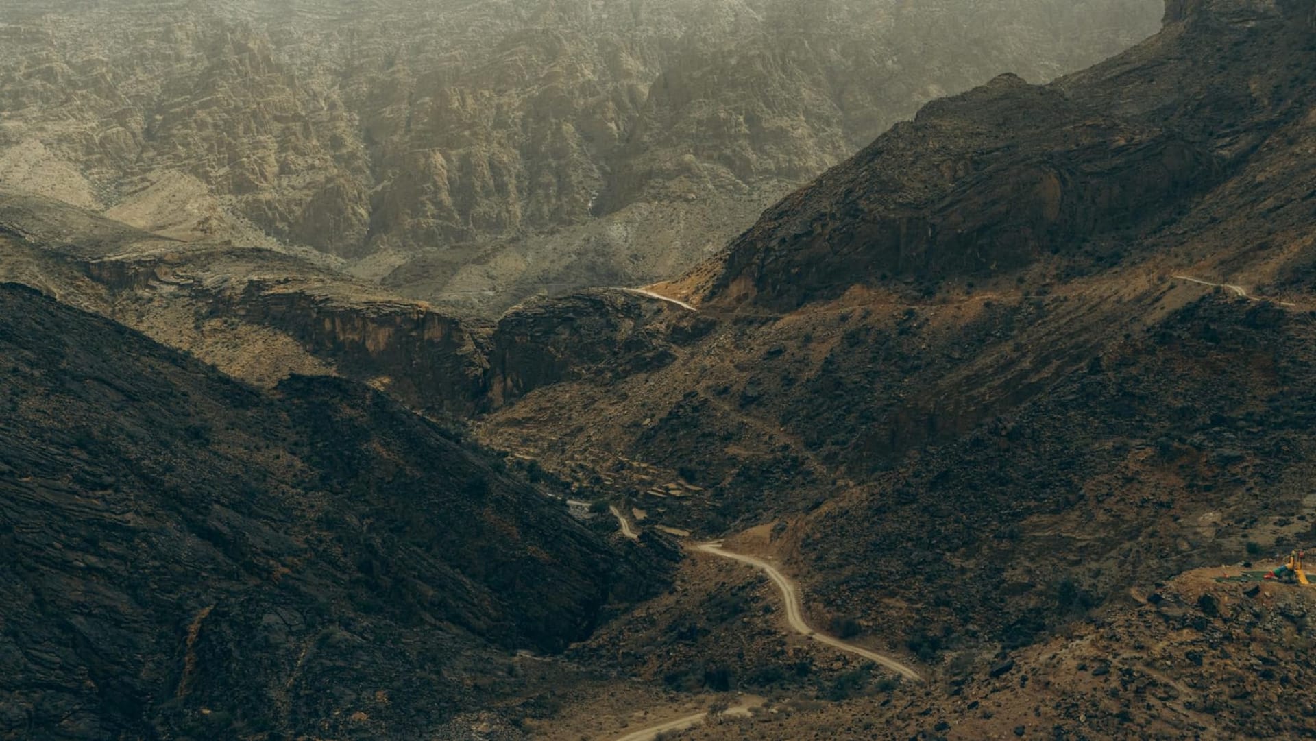 Ancient stone terraces carved into the cliffs of Jebel Akhdar with rose bushes in bloom and a village of ochre buildings stacked against the mountain face