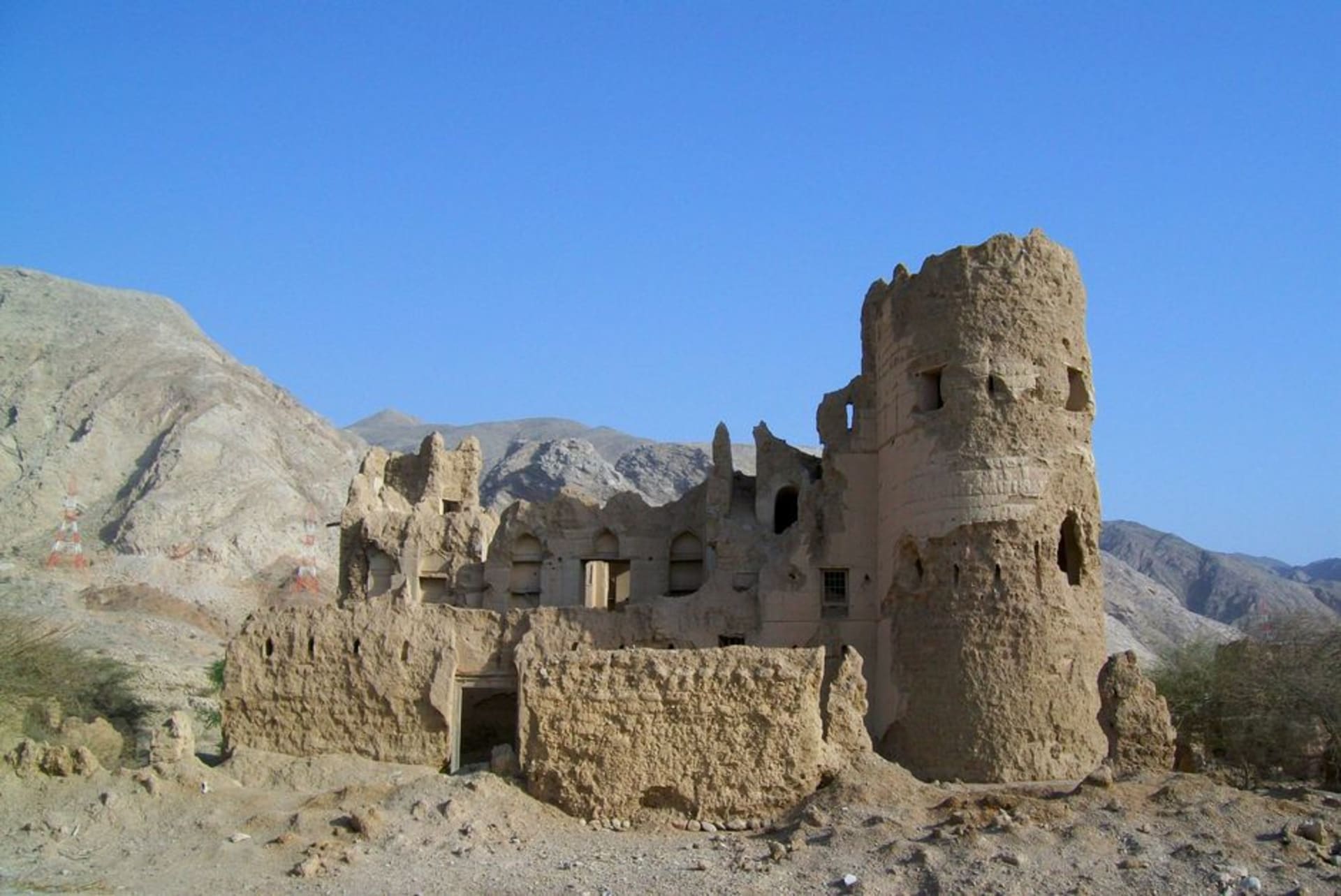 Collapsed mud-brick ruins of old Tanuf village scattered across a hillside, with palm trees and a wadi below