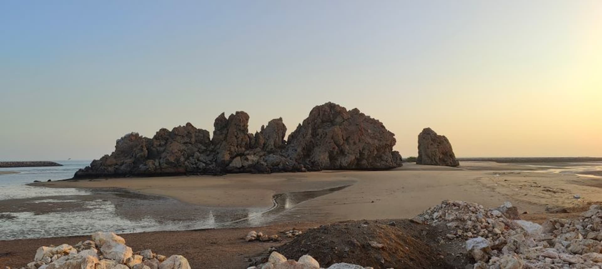 La amplia franja de arena pálida de la playa de Yiti respaldada por montañas pardas escarpadas, con botes pesqueros tradicionales varados en la orilla.
