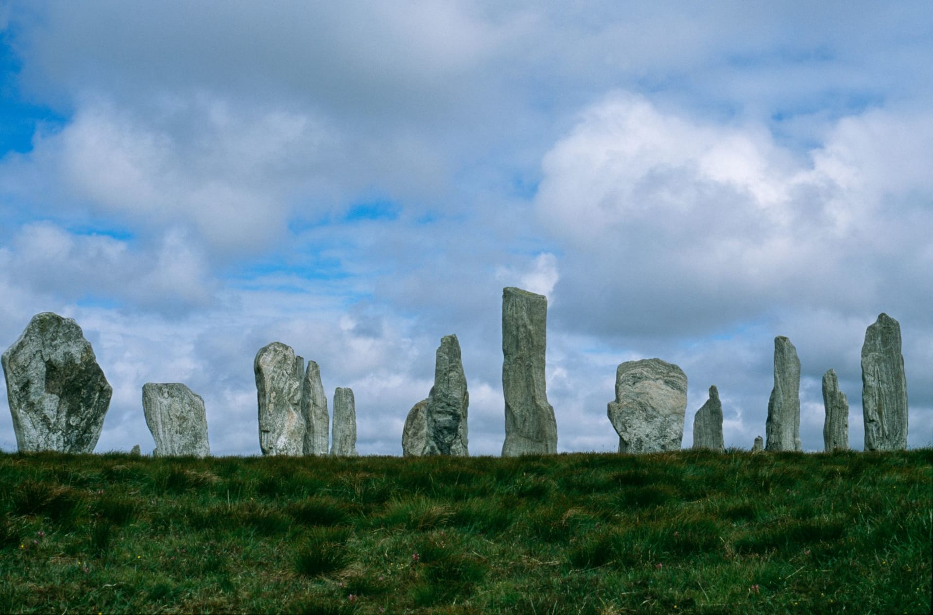 Eroded standing stones rising from open grassland beneath a dramatic cloudy sky in the Orkney Islands, Scotland