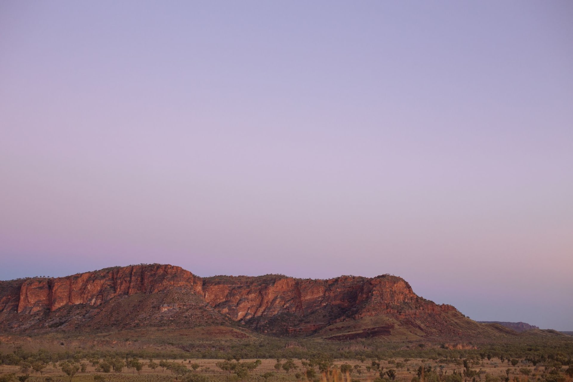 Orange and black striped sandstone beehive domes of Purnululu rising from a flat red Kimberley plain under a wide blue sky