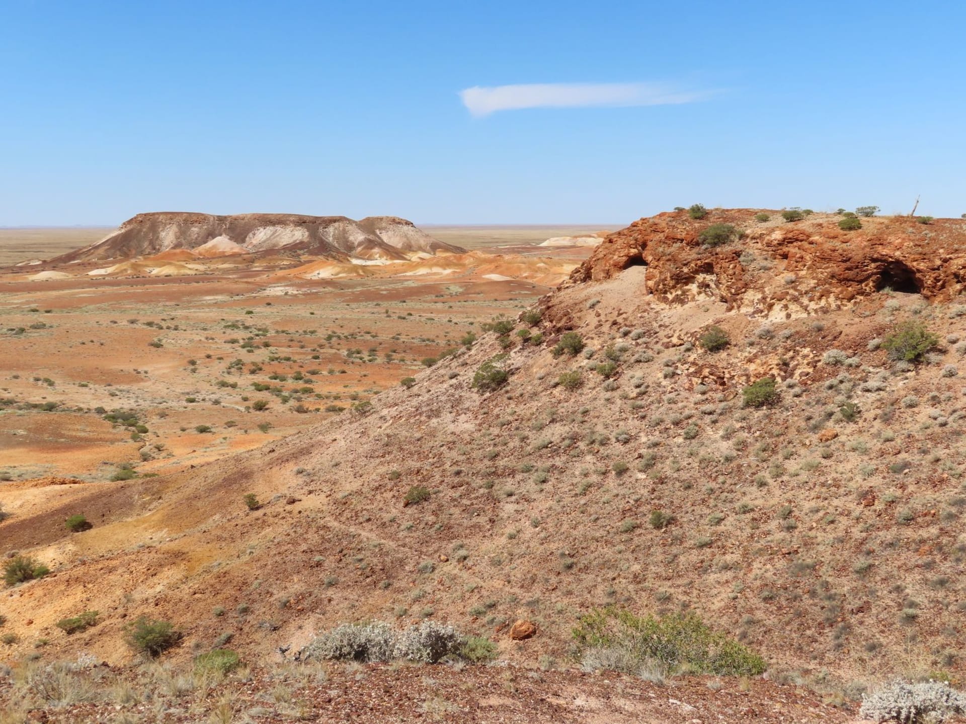 Dusty hillside of Coober Pedy with dugout homes carved into pale ochre earth under a blazing blue sky