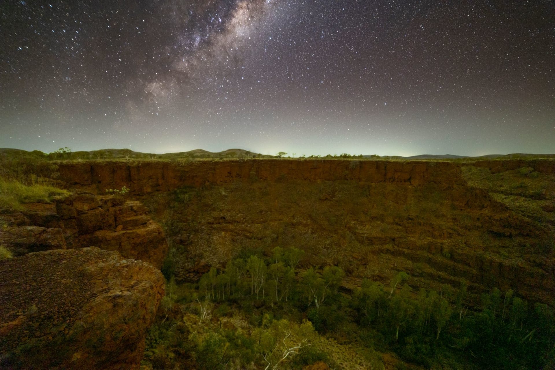 The Milky Way arching in vivid bands over the layered red rock walls of a gorge in Karijini National Park, Western Australia