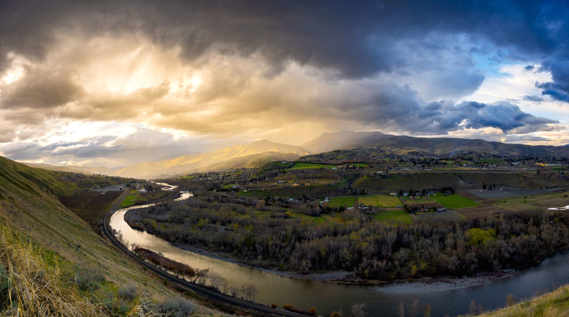 The Deschutes River running through downtown Bend at golden hour, Mt. Bachelor visible in the distance, kayakers on the whitewater section below the Old Mill