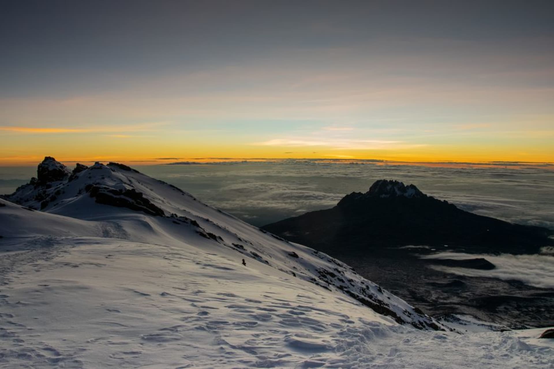 La cresta cumbre del Monte Wilhelm al amanecer, roca escarpada y pastizal alpino iluminados de dorado sobre un mar de nubes que llena los valles abajo