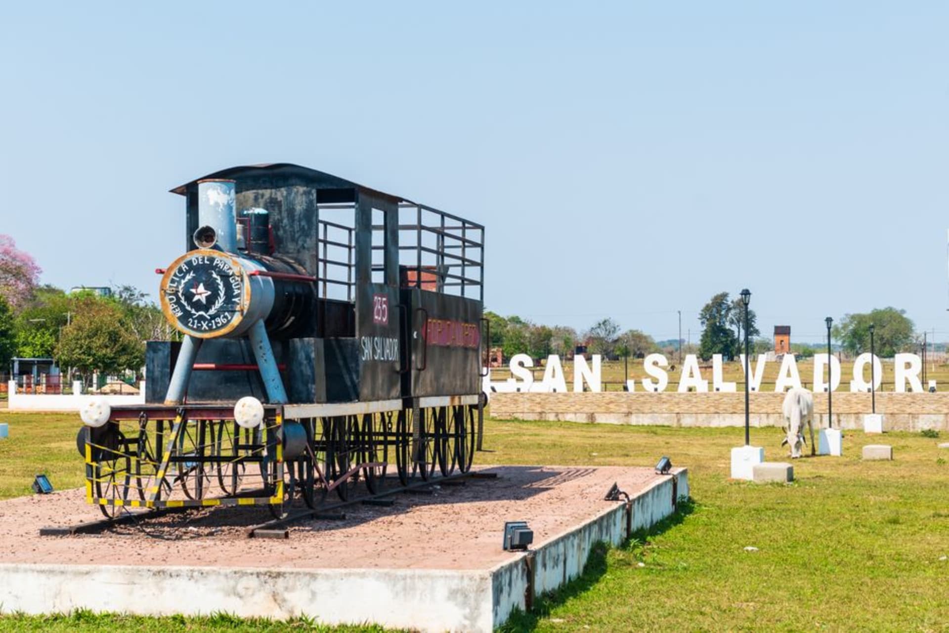 A weathered steam locomotive on display at the old railway station in Paraguari, hills rising green behind it