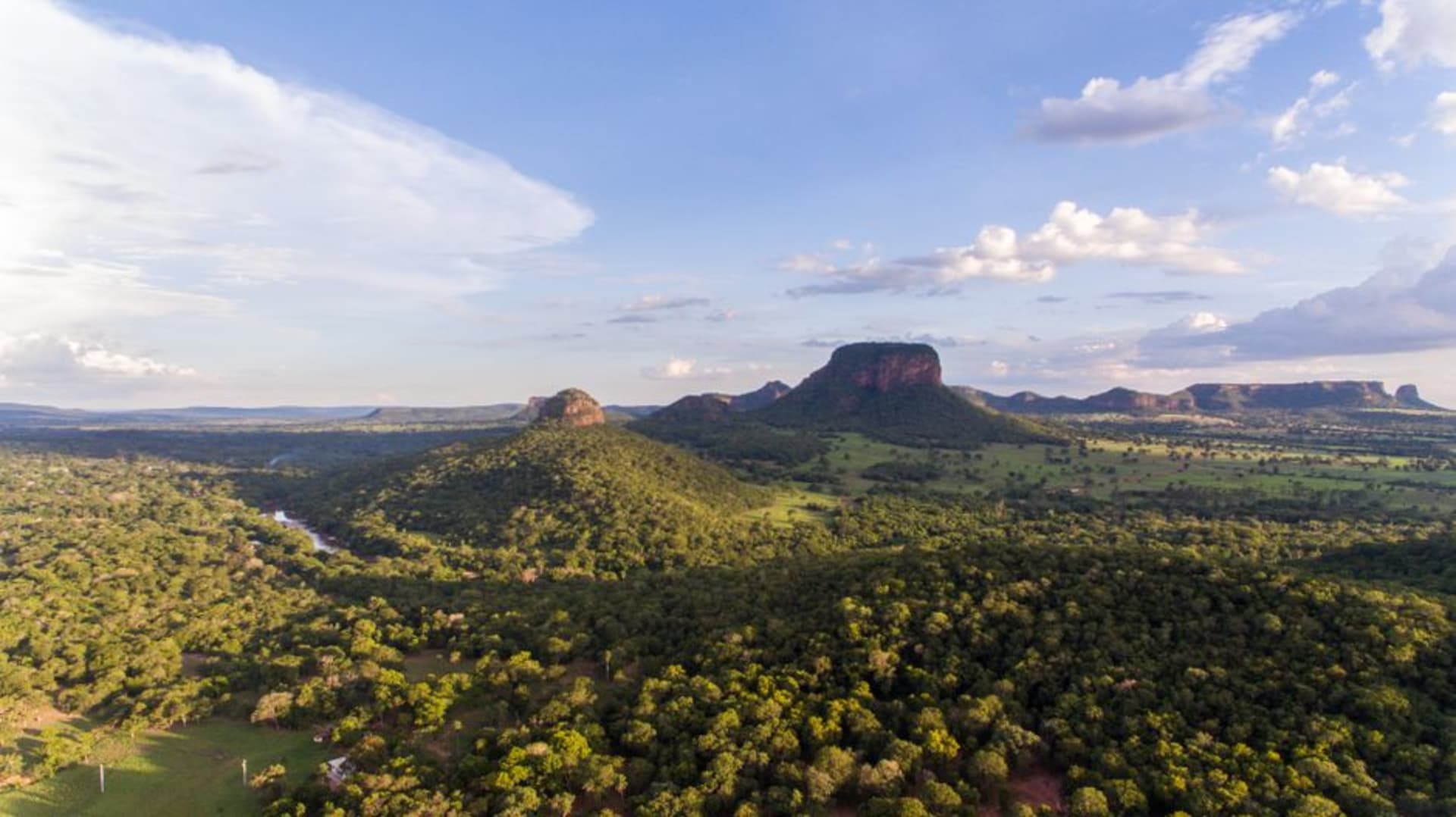 Picos boscosos de la sierra de Ybytyruzú alzándose sobre tierras de cultivo en el este de Paraguay bajo un cielo parcialmente nublado
