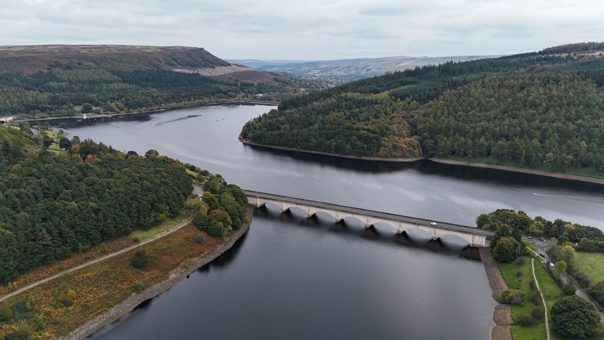 Ladybower Reservoir under a dramatic cloud sky, the dark water filling the valley between heather moorland slopes with the Derwent Edges visible above