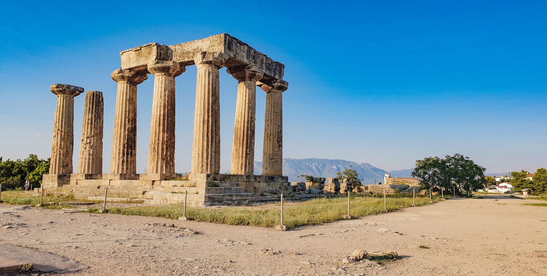 Seven columns of the Temple of Apollo at Ancient Corinth standing against the sky with Acrocorinth fortress rising behind them