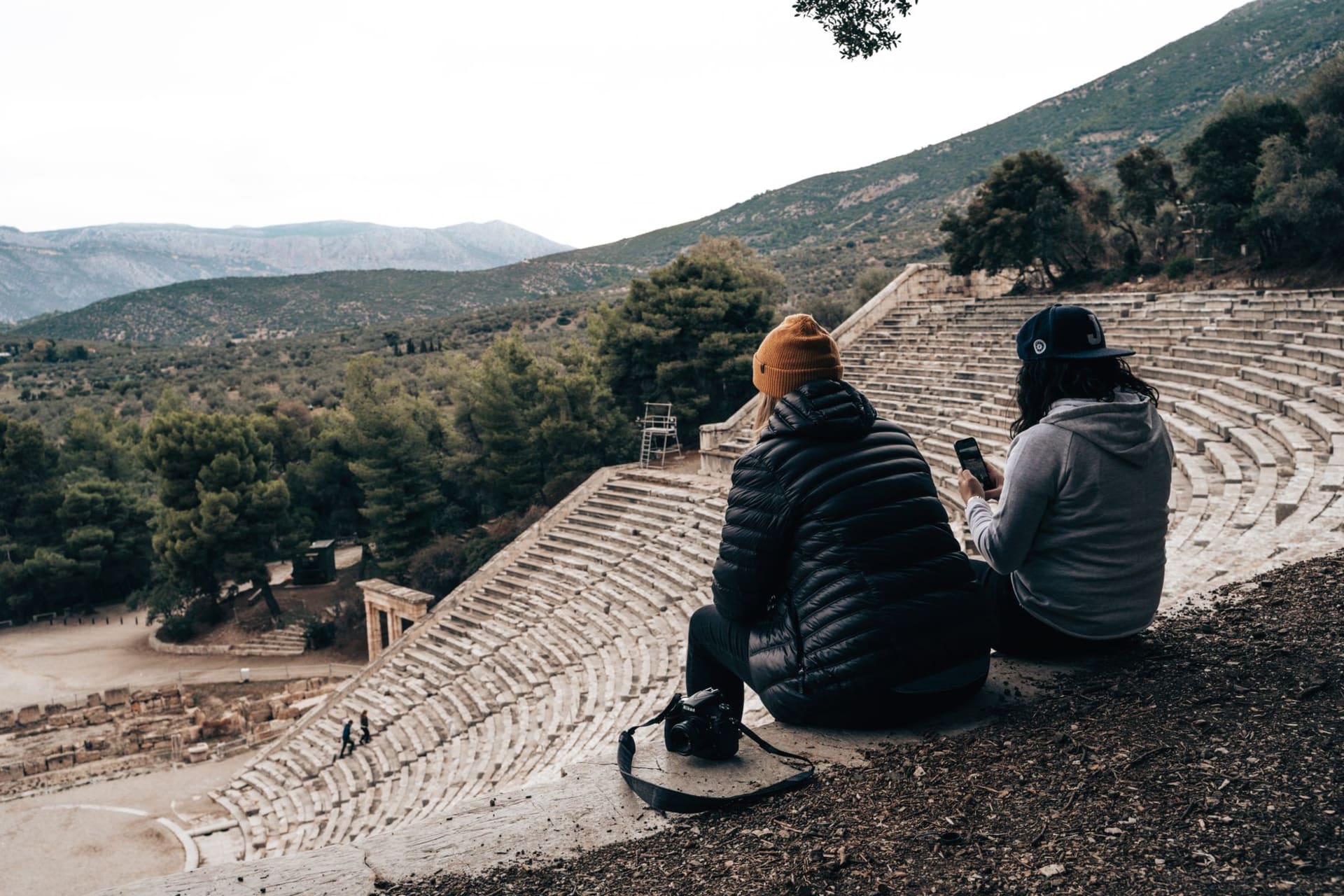The ancient theatre of Epidaurus seen from above, its limestone seats curving in perfect symmetry against the green hillside at dusk
