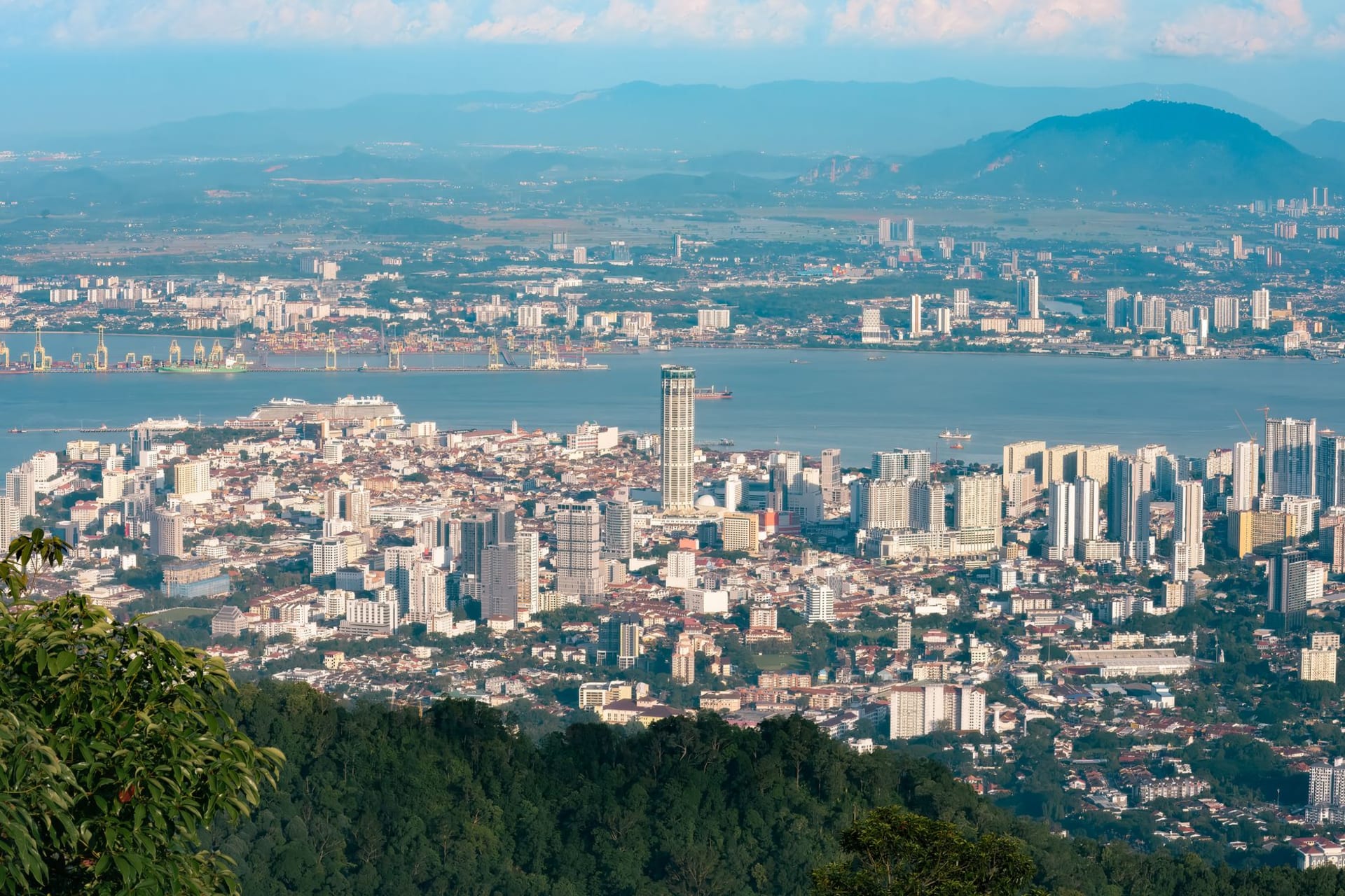 Forested slopes of Pulau Jerejak meeting the sea with the Penang Bridge in the distance, Malaysia
