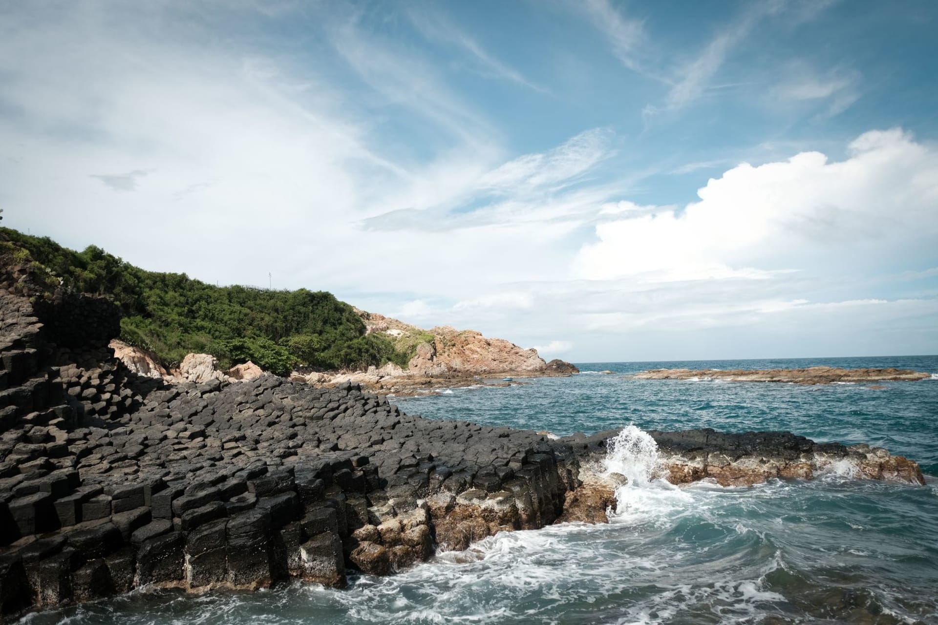 Ganh Dau cape with a narrow beach backed by dense forest, Cambodia's coast faintly visible across the water on the horizon