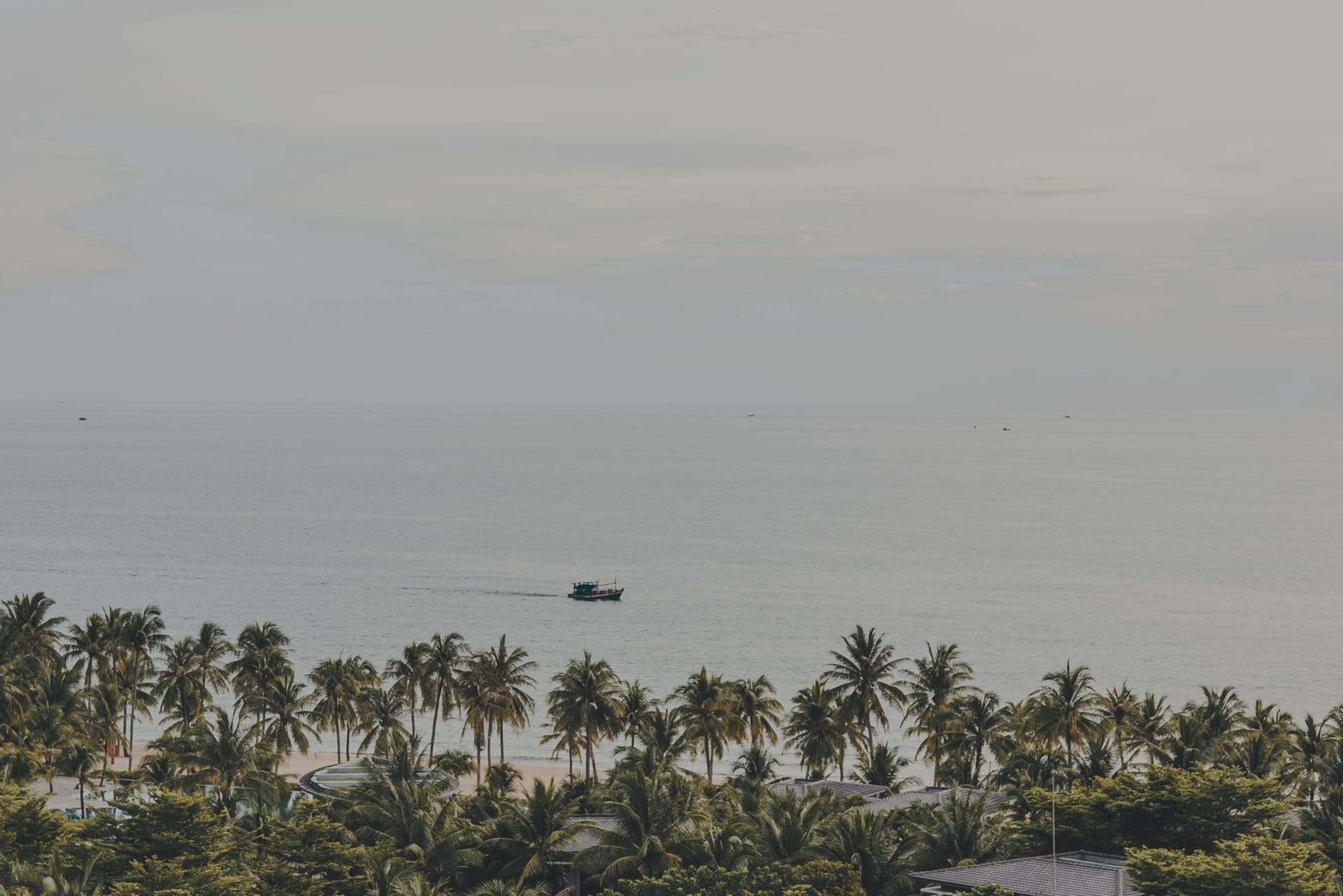 Palm-lined Phú Quốc beach with calm turquoise water and a fishing boat resting offshore