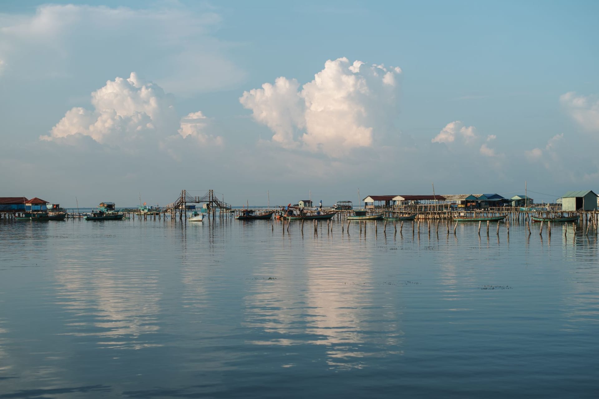 Rach Vem floating fishing village with wooden huts on pontoons at sunset, hills of the national park behind