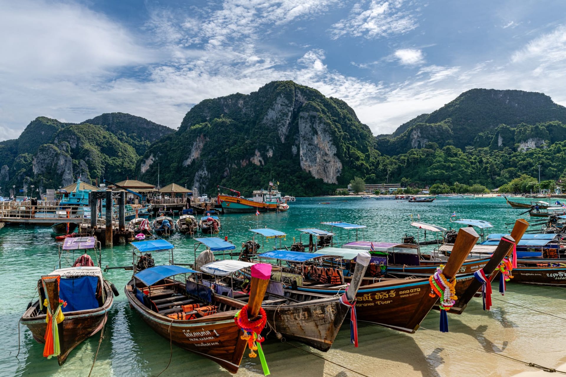 Colorful wooden longtail boats anchored in a turquoise bay ringed by jungle-covered hills in Phuket, Thailand