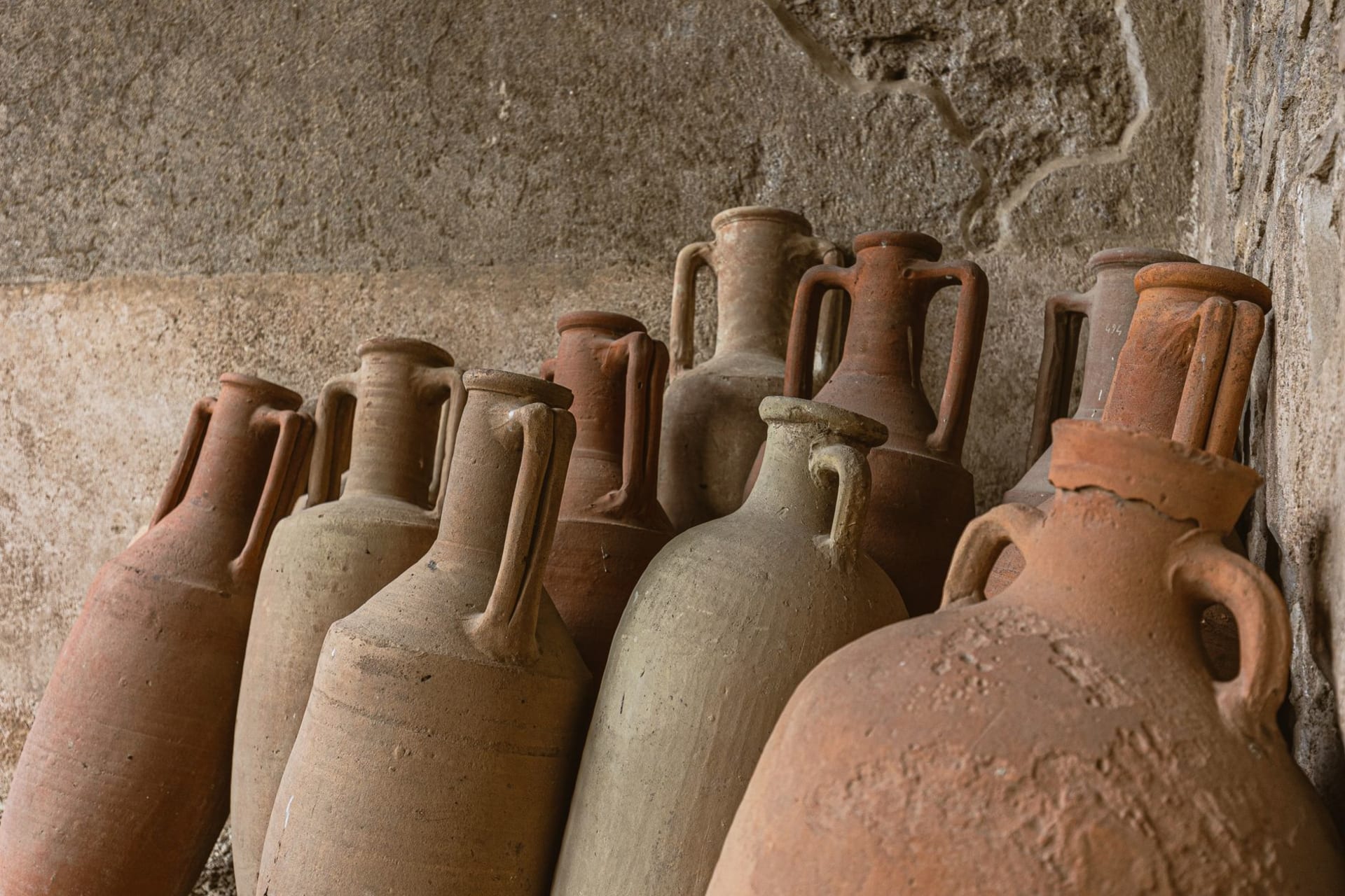 Rustic ancient clay jars arranged against a textured stone wall in warm light