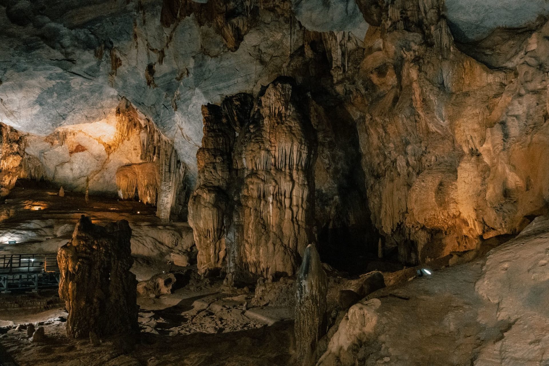 The entrance to Tham Piu Cave high in a limestone cliff face above a forested valley, flags and offerings visible at the mouth