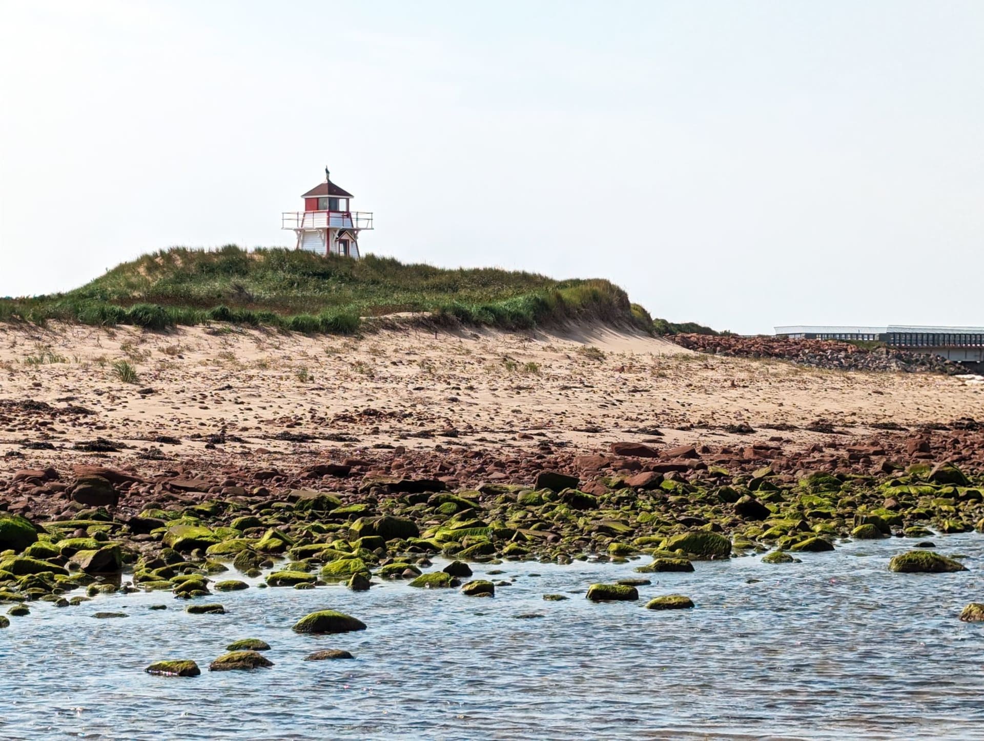 The round red-and-white brick Point Prim Lighthouse standing on a low grassy headland above the Northumberland Strait, Prince Edward Island