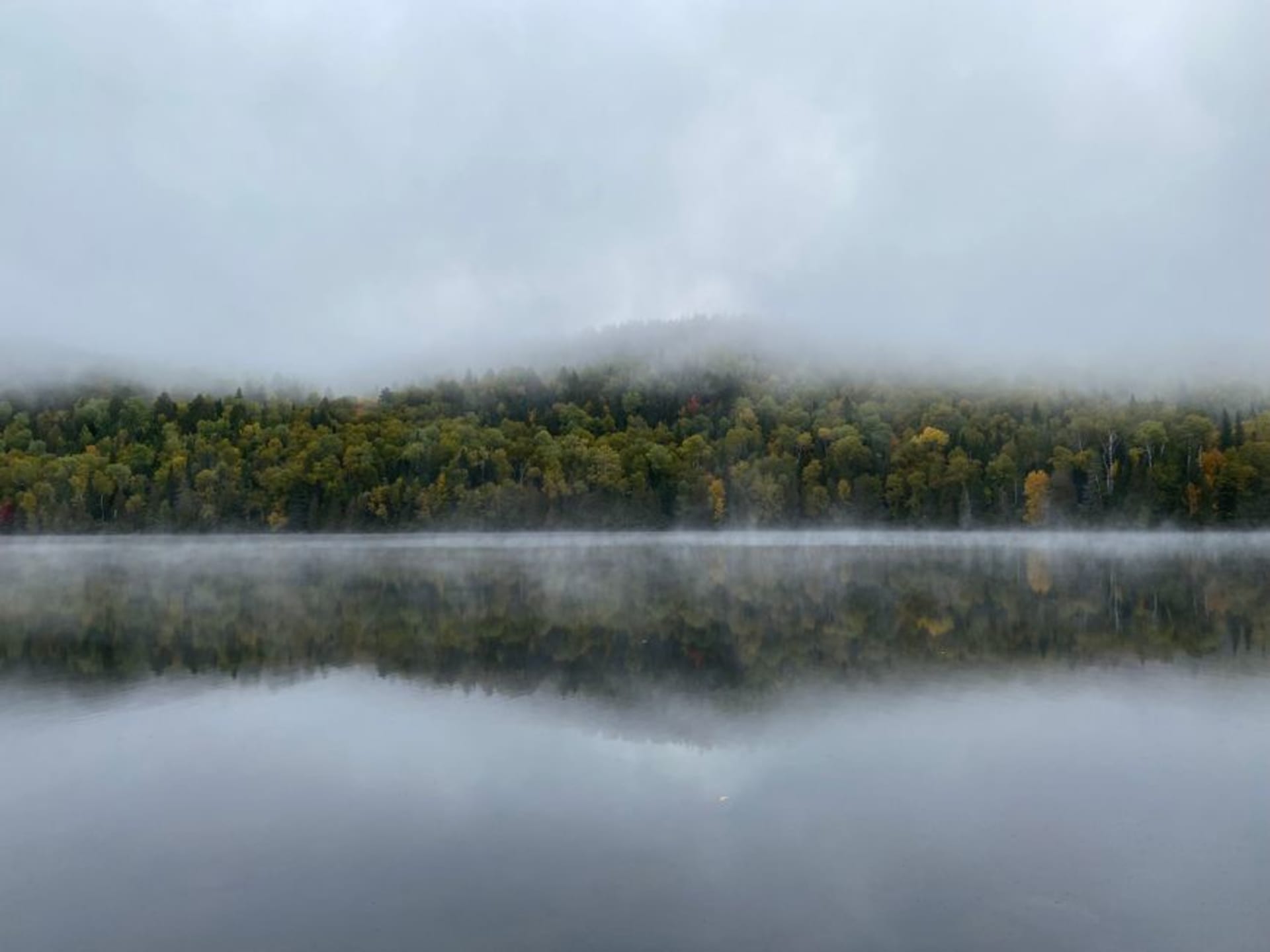 Una canoa deslizándose sobre aguas quietas en Parc National de la Mauricie al amanecer, niebla elevándose del lago entre colinas boscosas