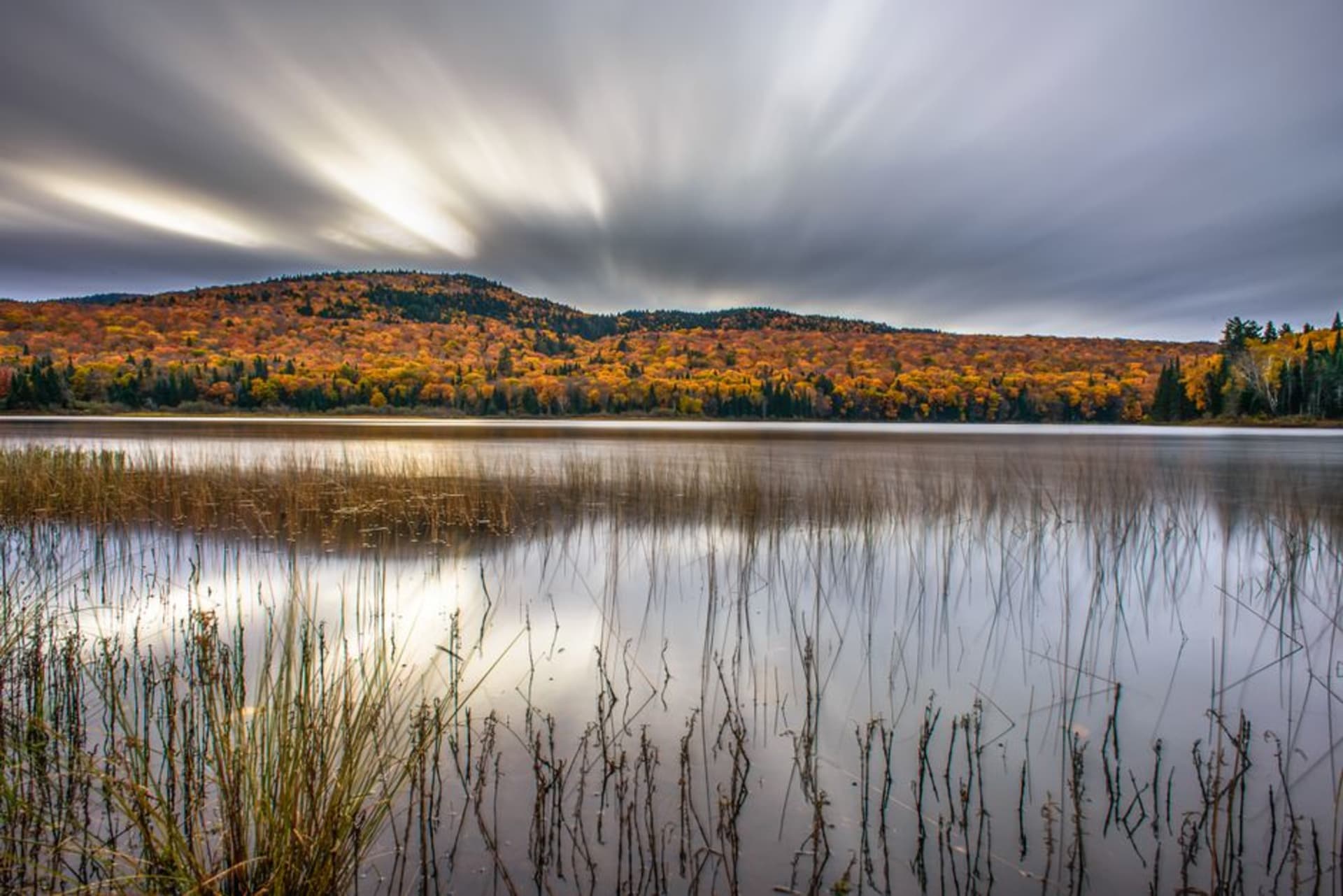Niebla elevándose de un lago quieto al amanecer en Parc national du Mont-Tremblant, colinas boscosas reflejadas en el agua