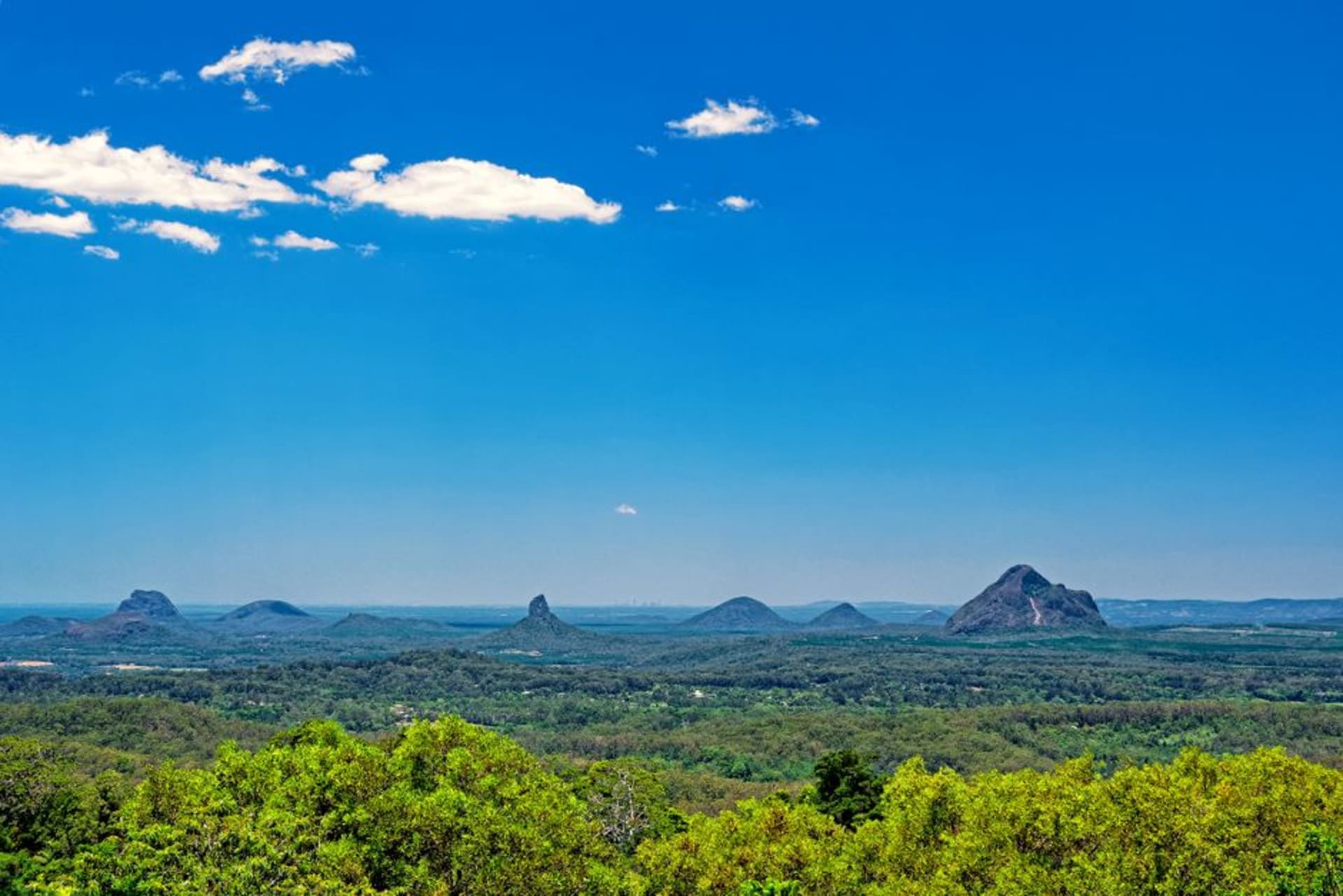 Los picos volcánicos de las Glass House Mountains elevándose sobre tierras de cultivo verdes bajo un cielo de amanecer pastel