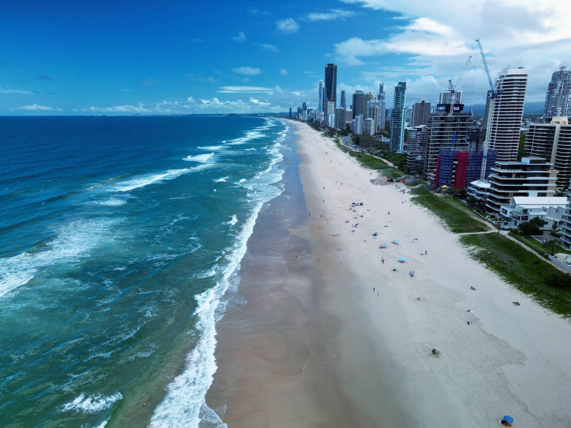 Burleigh Heads point break on a clear morning, clean surf running south, the distant towers of Surfers Paradise visible up the coast