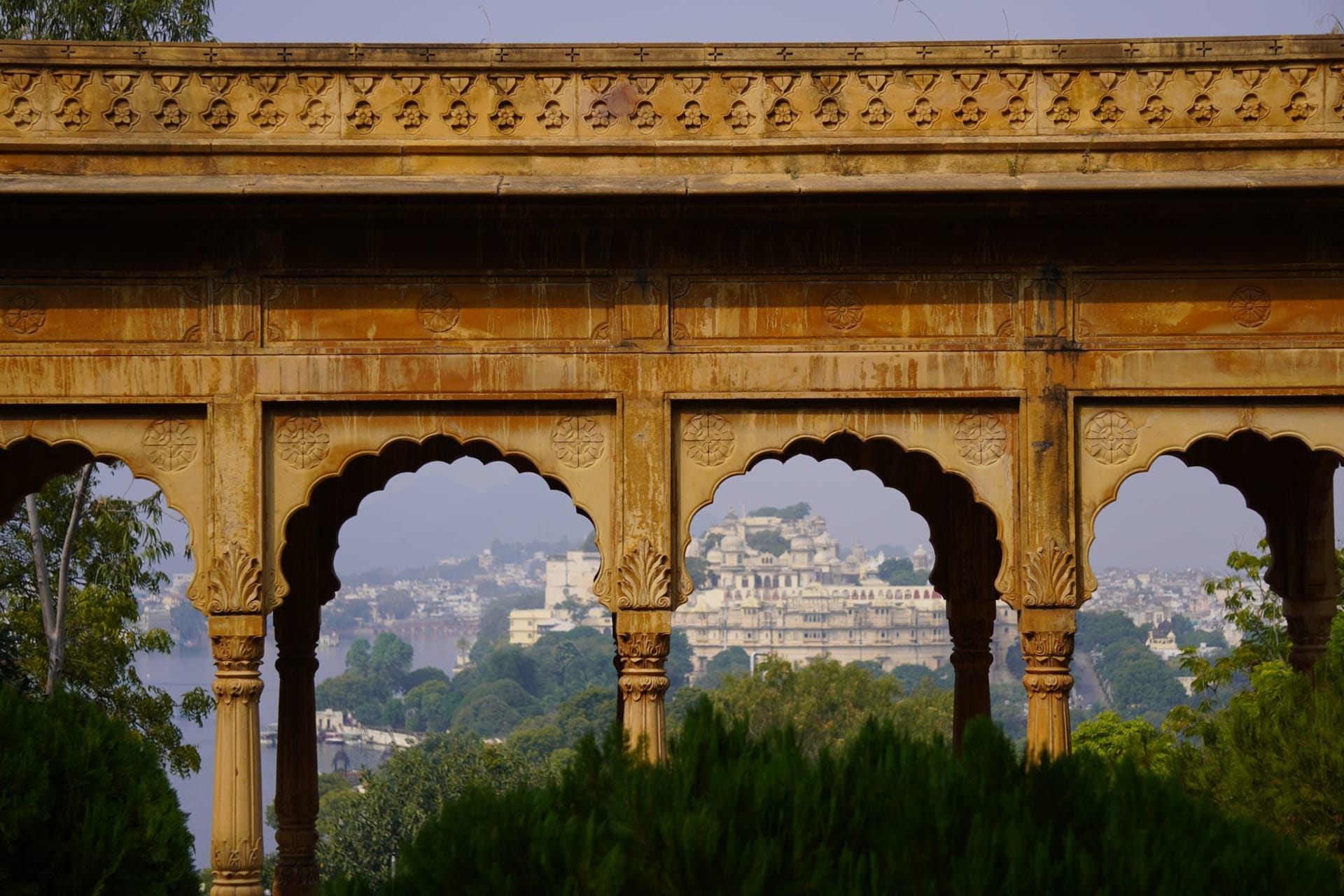 Udaipur's City Palace rising white and gold above the glassy morning waters of Lake Pichola, with the Lake Palace visible mid-water