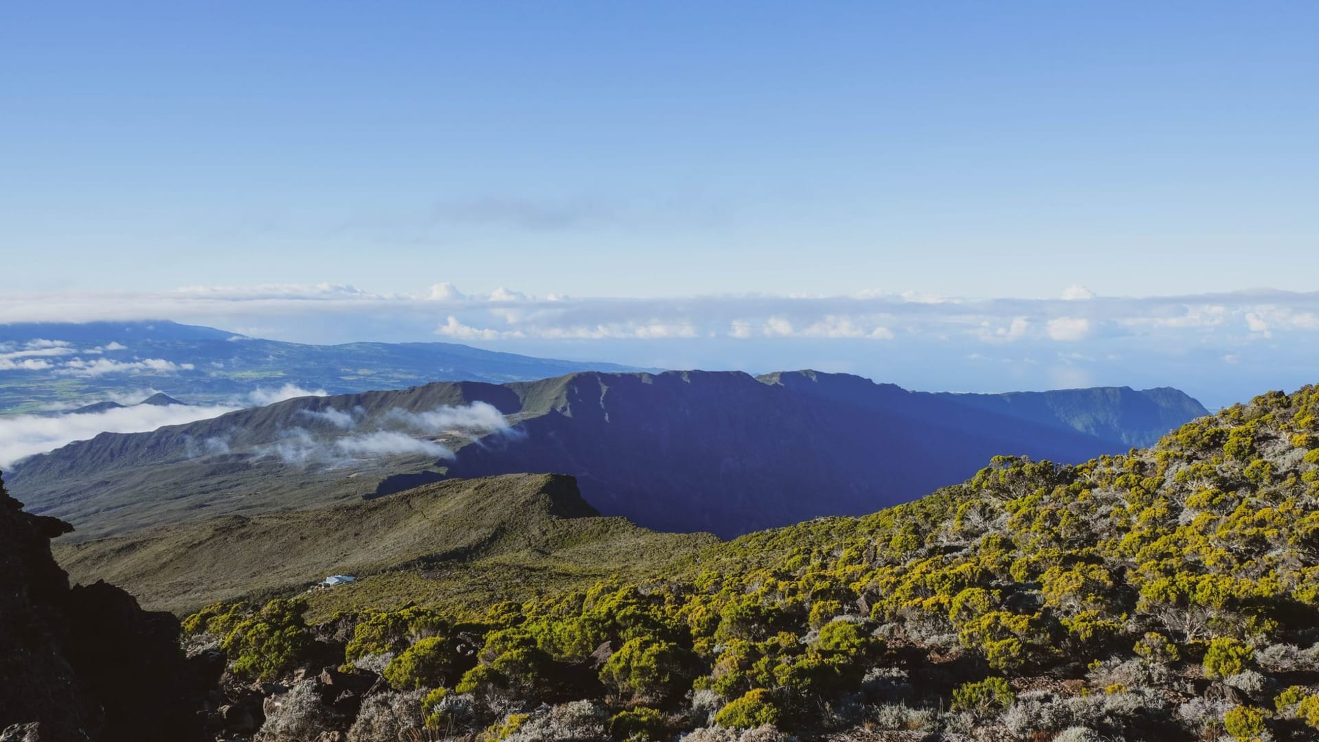 Vista aérea del paisaje volcánico de la isla Reunión — campos de lava oscura cortando la densa vegetación tropical bajo un cielo abierto