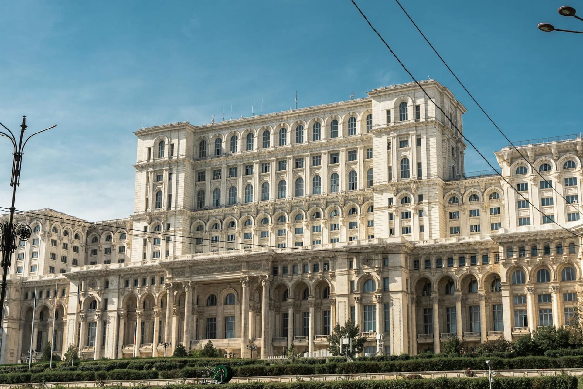 The colossal facade of the Palace of Parliament rising above Bucharest's wide boulevards at dusk, its limestone columns catching the last orange light of the day