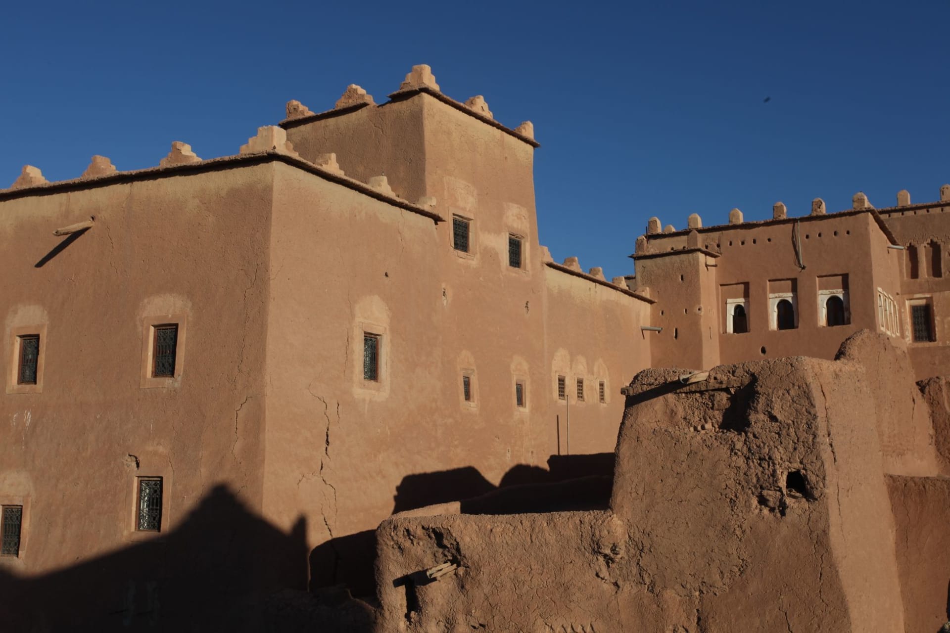 Ksar Aït Benhaddou, ancient fortified village near Ouarzazate, glowing amber against blue sky in late afternoon light