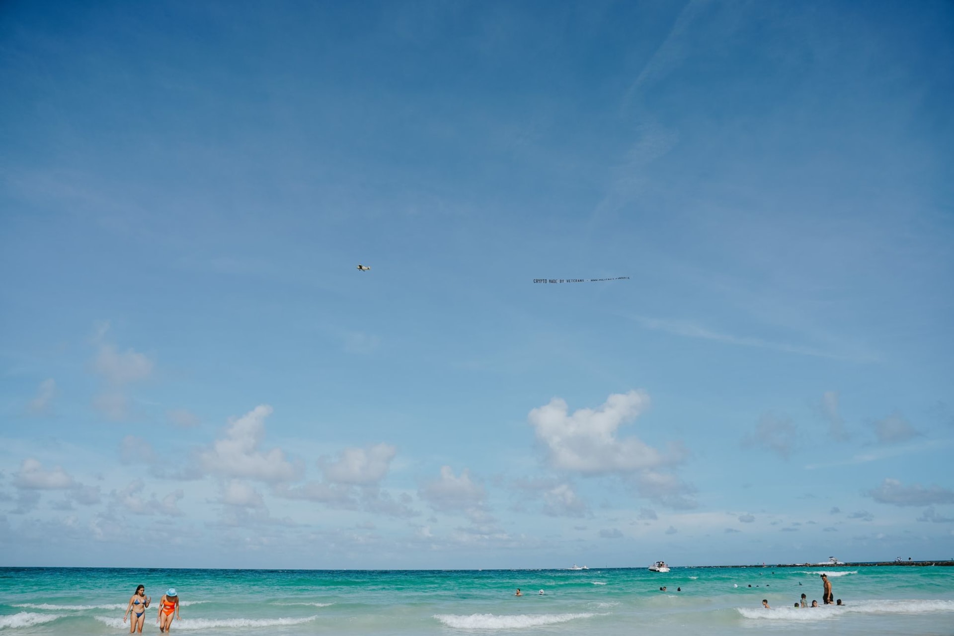 A large commercial aircraft descending just above the heads of sunbathers on Maho Beach, its shadow falling on the pale sand below