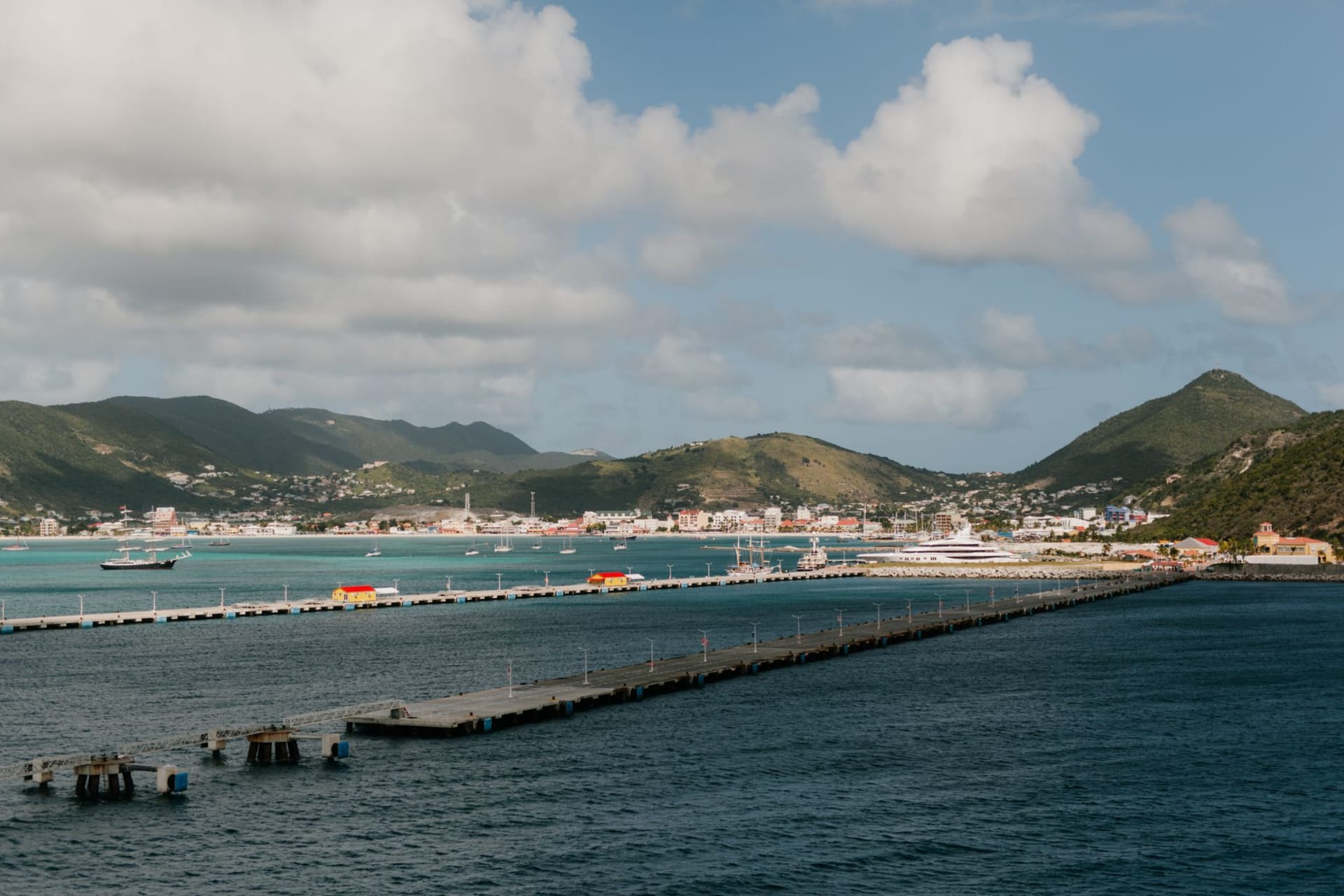 The covered market arcade in Marigot on a Saturday morning, stalls of spices and vegetables in warm tropical light, Fort Louis ruins on the hill above