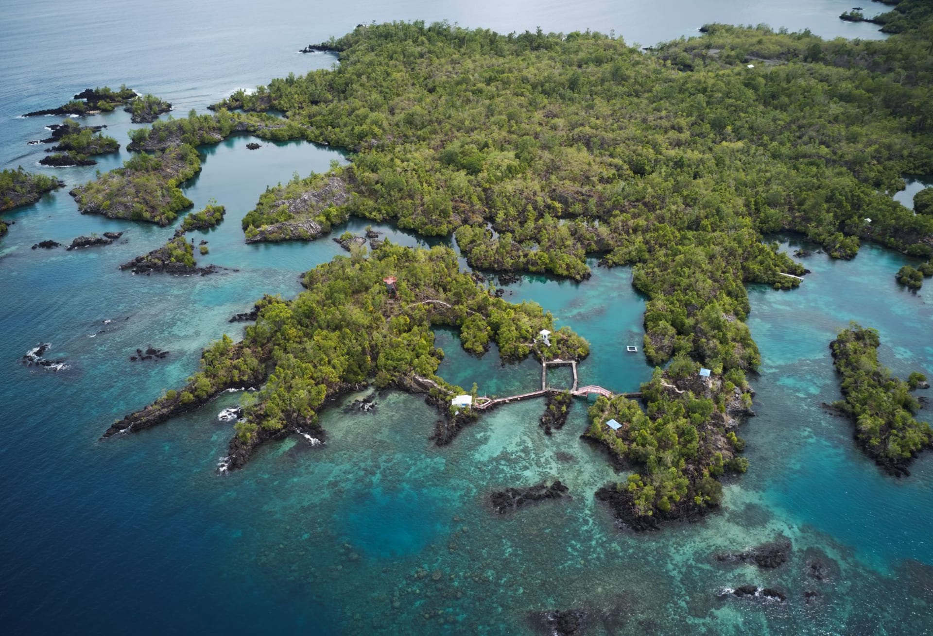 L'île Manono vue depuis l'eau, basse et verte, ceinturée par le récif, un fale de village visible à l'ombre des palmiers le long du rivage