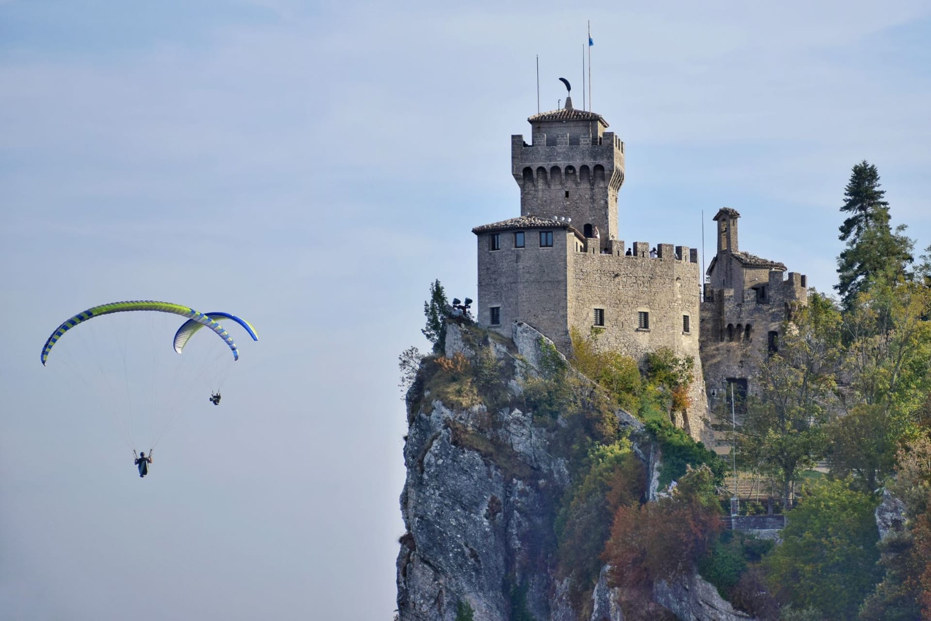La Guaita tower rising from the limestone cliff of Monte Titano at sunrise, its medieval walls glowing amber against a deep blue sky