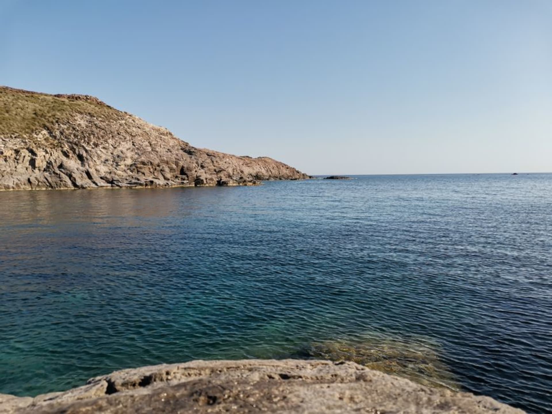 Le littoral de l'île de Sant'Antioco, avec une eau claire et des rives rocheuses sous un ciel sarde lumineux