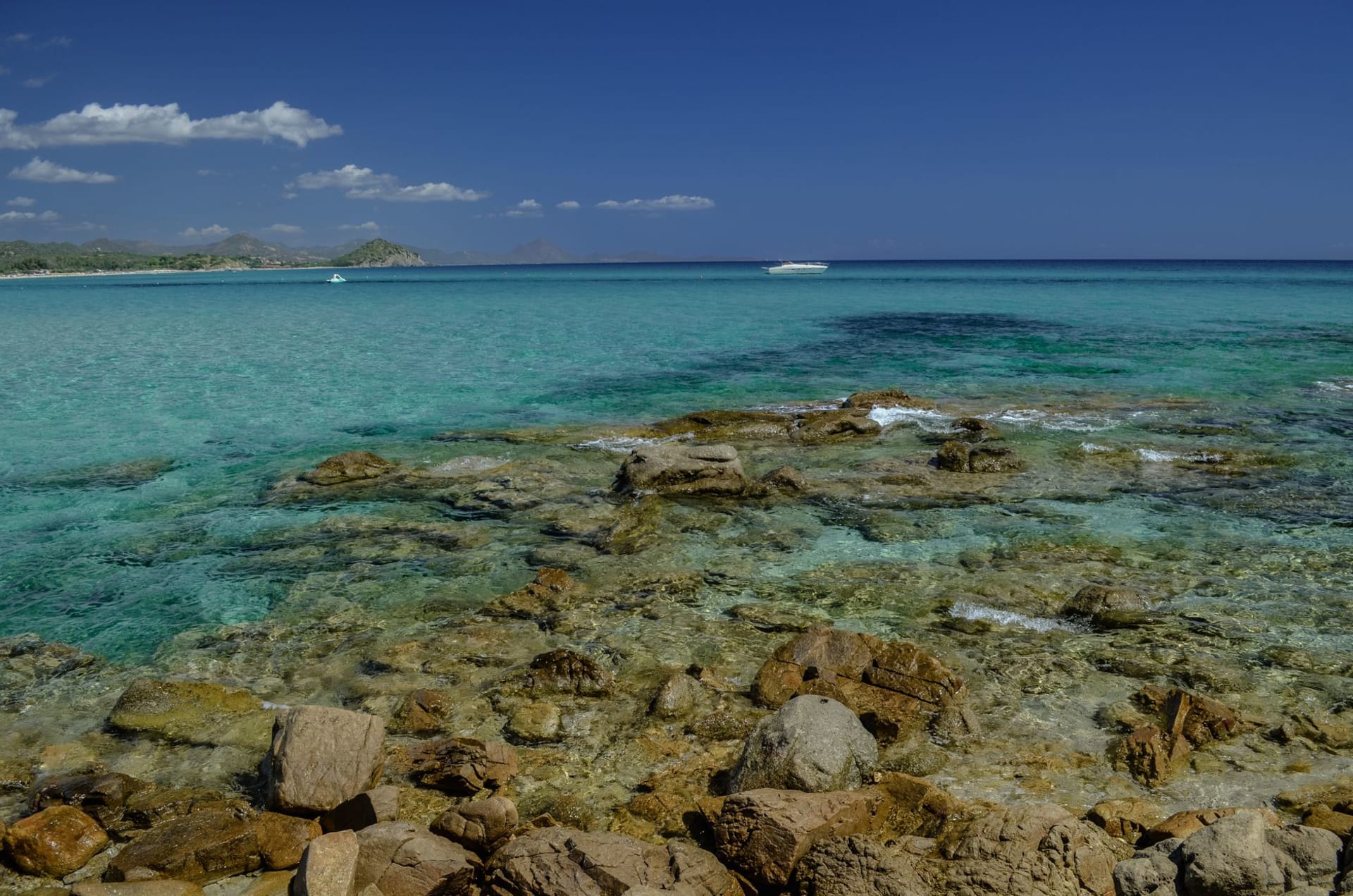 Clear turquoise waters washing over rocky Sardinian shoreline under a bright blue sky