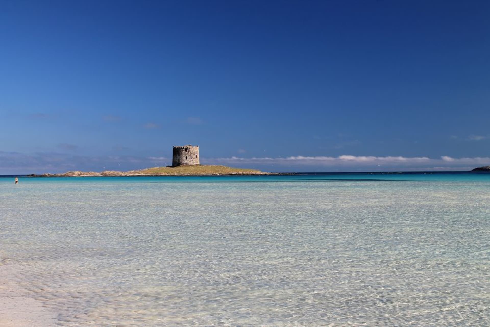 The turquoise shallow water and white sand of Spiaggia della Pelosa near Stintino with a small Aragonese tower offshore