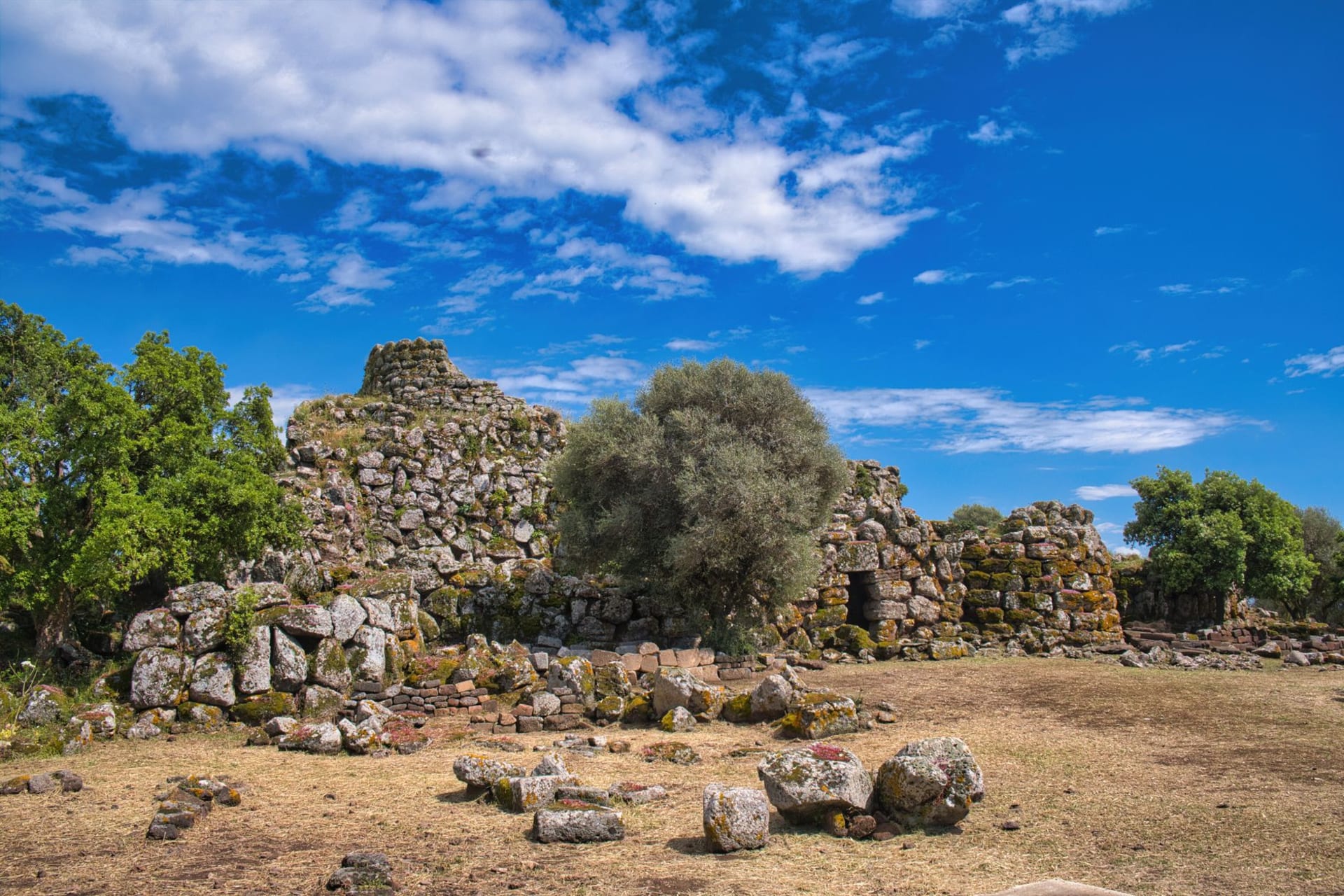 The conical stone central tower of Su Nuraxi di Barumini rising above a maze of low Bronze Age walls under a hot blue Sardinian sky