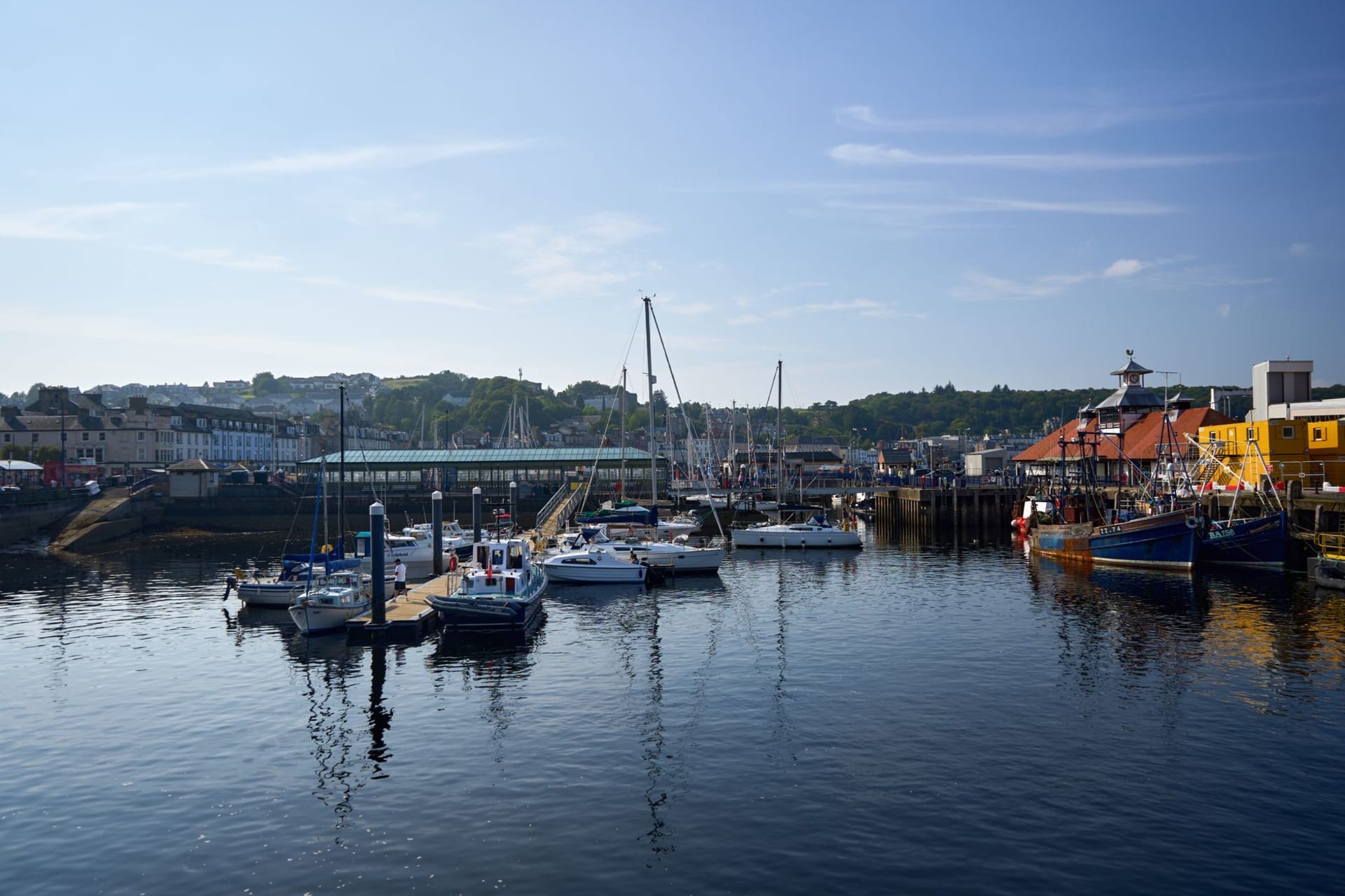 Oban harbour at dusk with colorful fishing boats moored along the pier and the colosseum-like arches of McCaig's Tower silhouetted on the hill above the town lights
