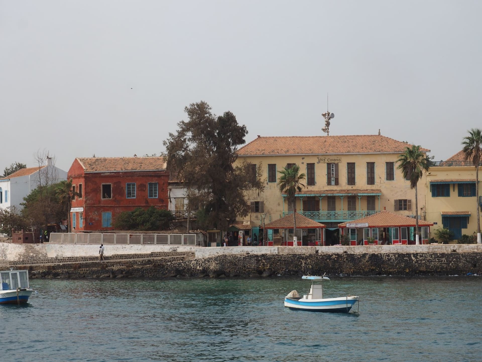 Pastel colonial facades on Île de Gorée with bougainvillea cascading over an ochre wall and the deep blue Atlantic visible at the end of the narrow street