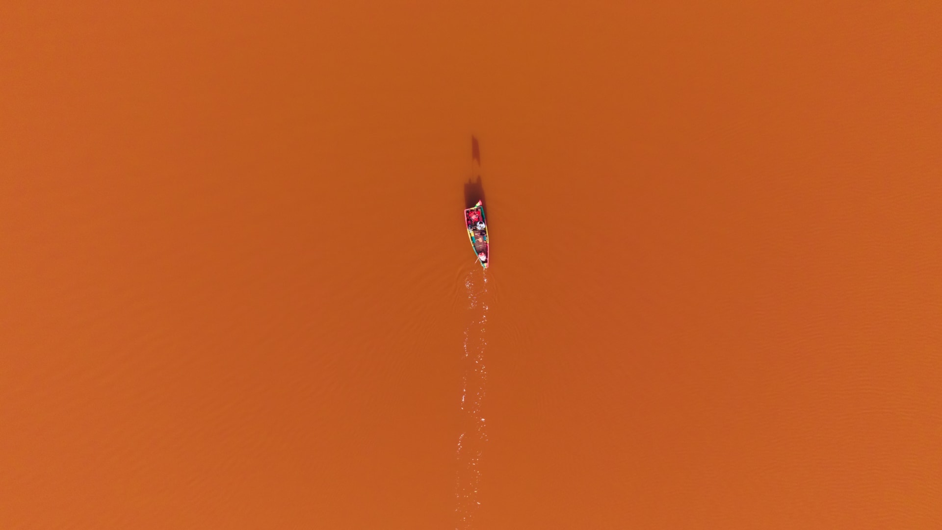 Aerial view of a colorful wooden canoe crossing the vivid orange-pink waters of Lake Retba, Senegal