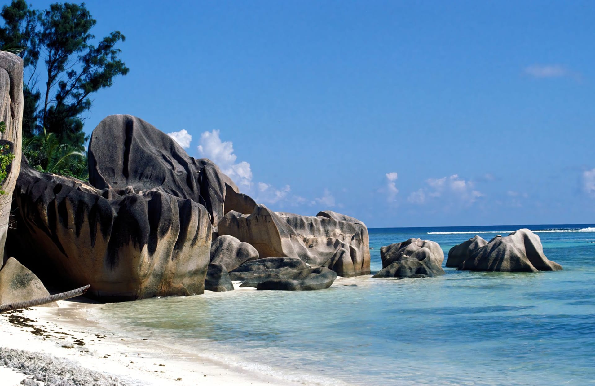 Massive pink granite boulders framing a pristine white-sand beach on La Digue, Seychelles, with vivid turquoise water under a clear blue sky