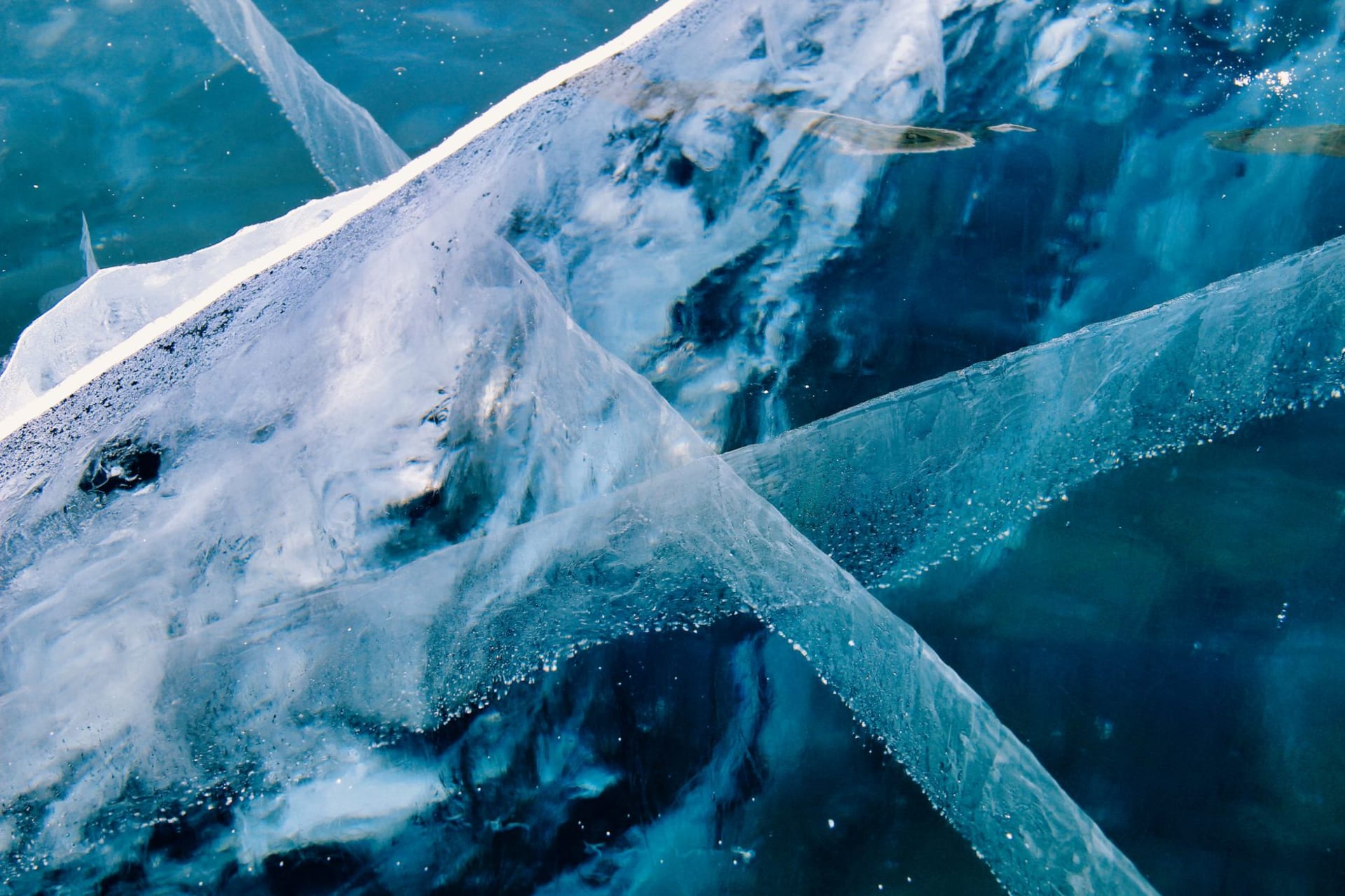 Lake Baikal's impossibly blue water stretching to distant mountains under a pale winter sky, with translucent green ice in the foreground