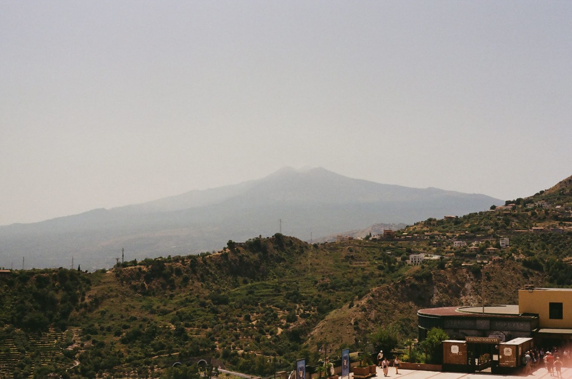 Scenic view of Mount Etna looming behind the terracotta rooftops of Taormina, captured in warm film tones