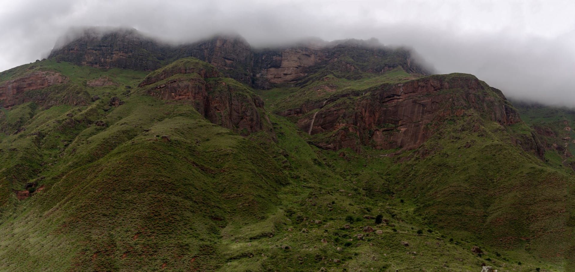 A solitary figure standing on a narrow rock promontory above the clouds, the Simien escarpment curving away in both directions into pale morning haze