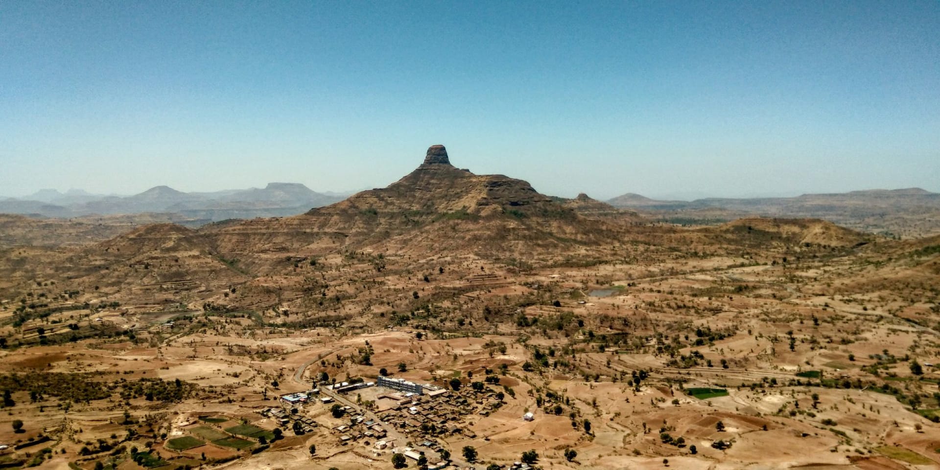 The rocky summit ridge of Silki Yared at 4,420 meters, a single Ethiopian wolf visible as a rust-red shape on the plateau below, the Simien massif behind