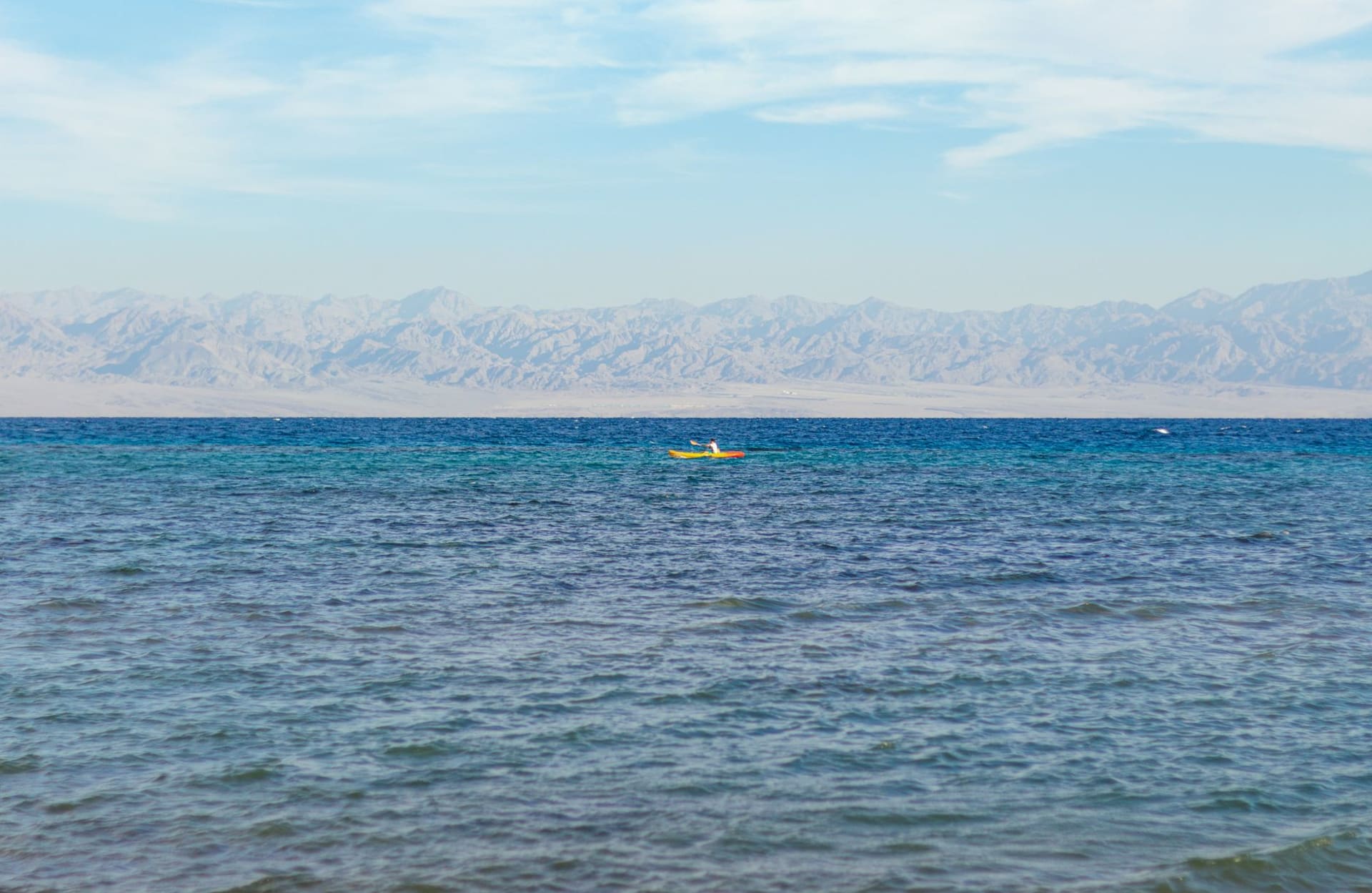 Un campement de plage bédouin au crépuscule à Nuweiba, avec de basses huttes de chaume sur une plage de sable blanc et les montagnes jordaniennes rougeoyant en ambre de l'autre côté du golfe d'Aqaba